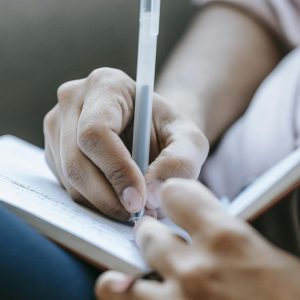 Crop anonymous person taking notes in diary placed on laps in light room