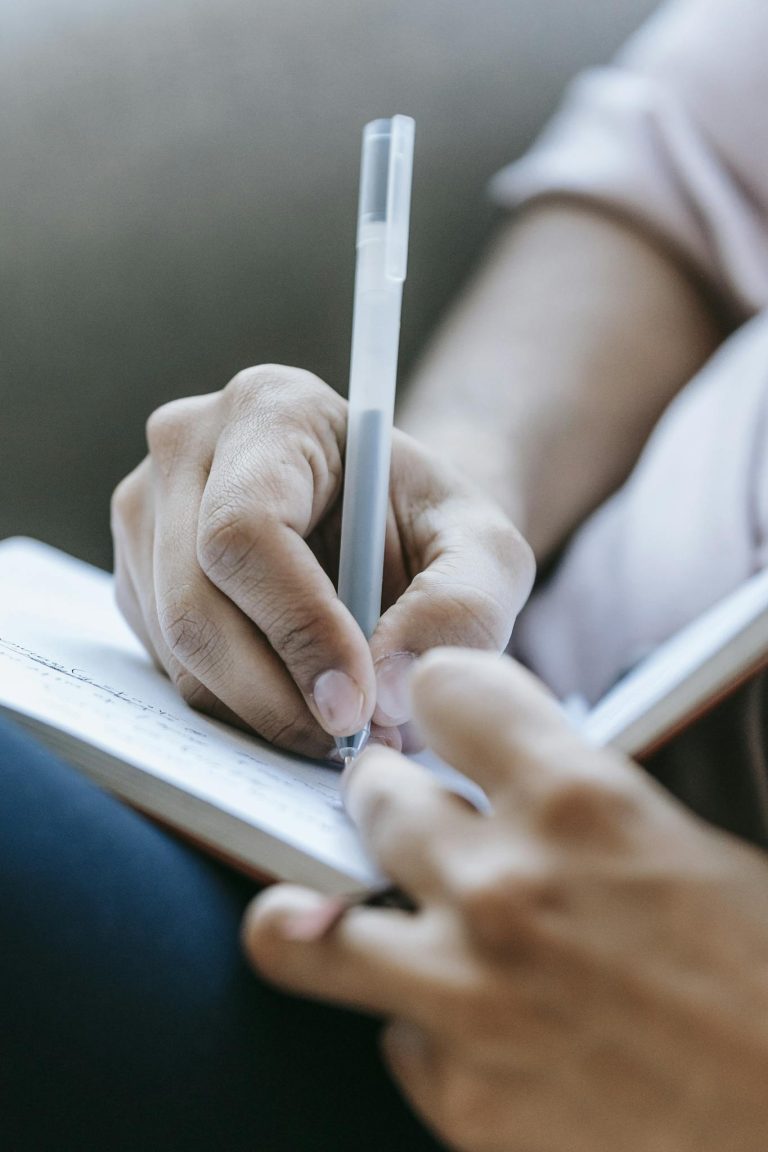 Crop anonymous person taking notes in diary placed on laps in light room