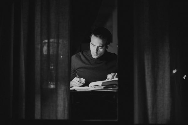 Pensive man writing in notebook and reading book